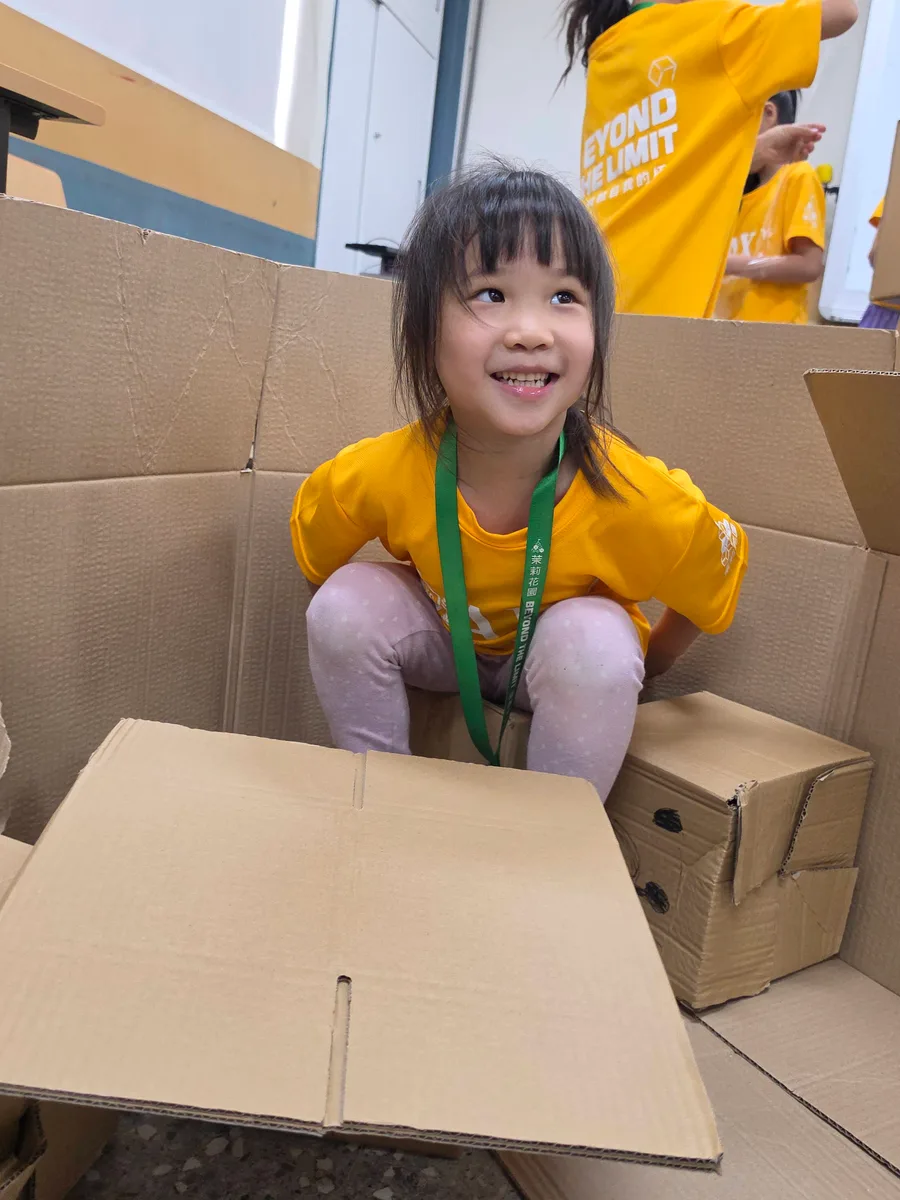 孩子坐在紙箱作品中，抬頭和夥伴互動