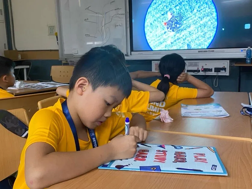 孩子在紙上畫圖，後方螢幕顯示放大的影像