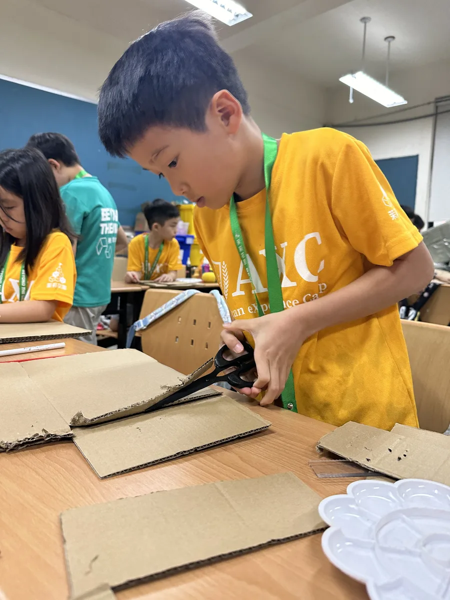 孩子專注地剪裁紙板，準備建造材料