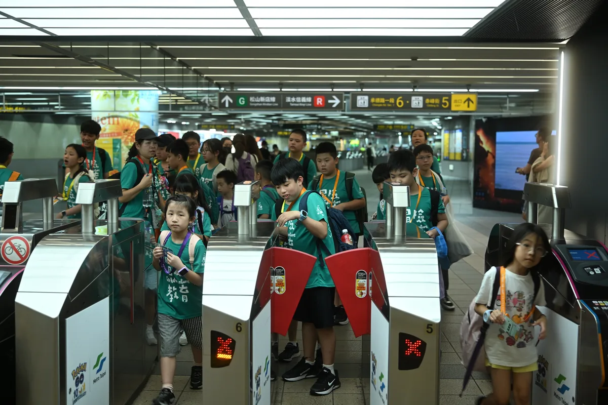 孩子背著背包、拿票卡通過捷運閘門，領隊與隊友在旁