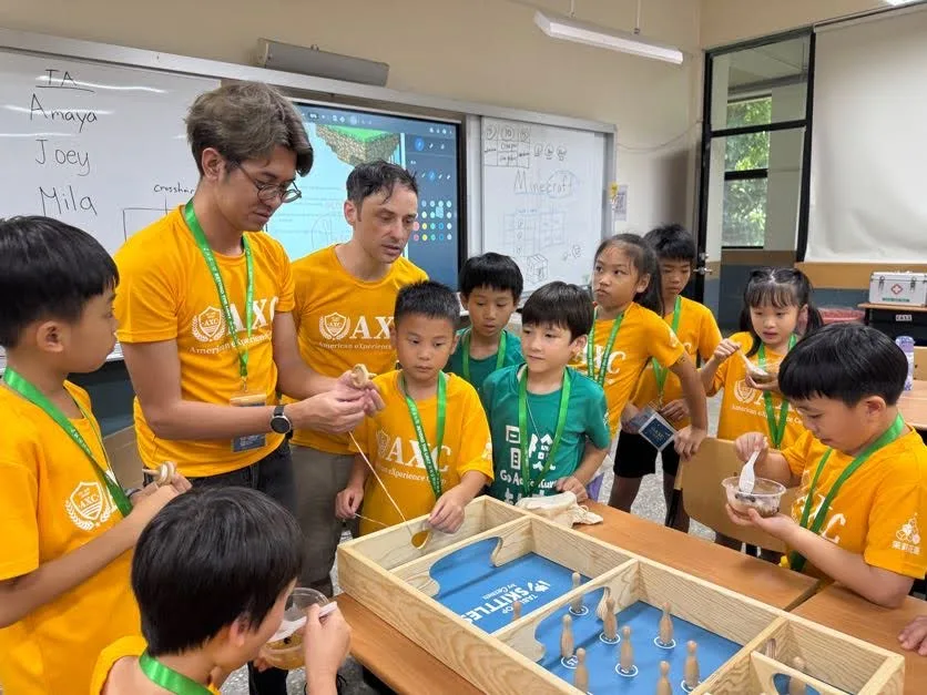 外師與助教和孩子們圍在桌邊，一起動手操作木製裝置