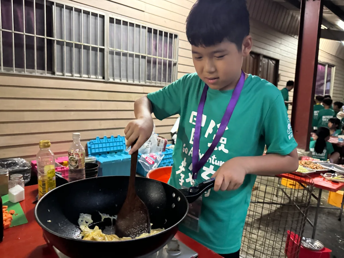 孩子握住鍋柄，用鍋鏟翻動鍋中的食物